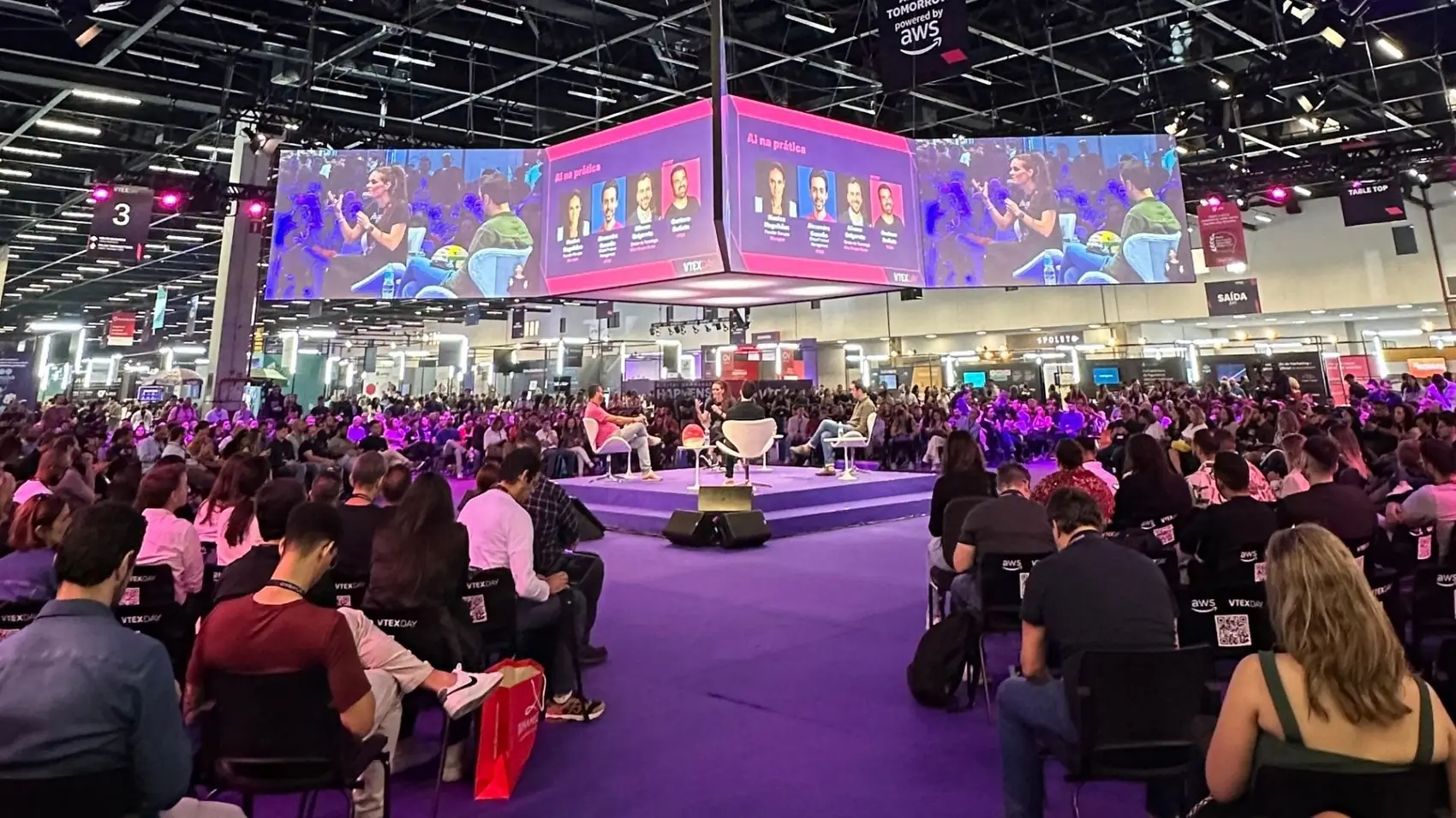 Panel with Monica Magalhaes on the main stage of a technology event, facing a packed audience, with her image projected on the screens