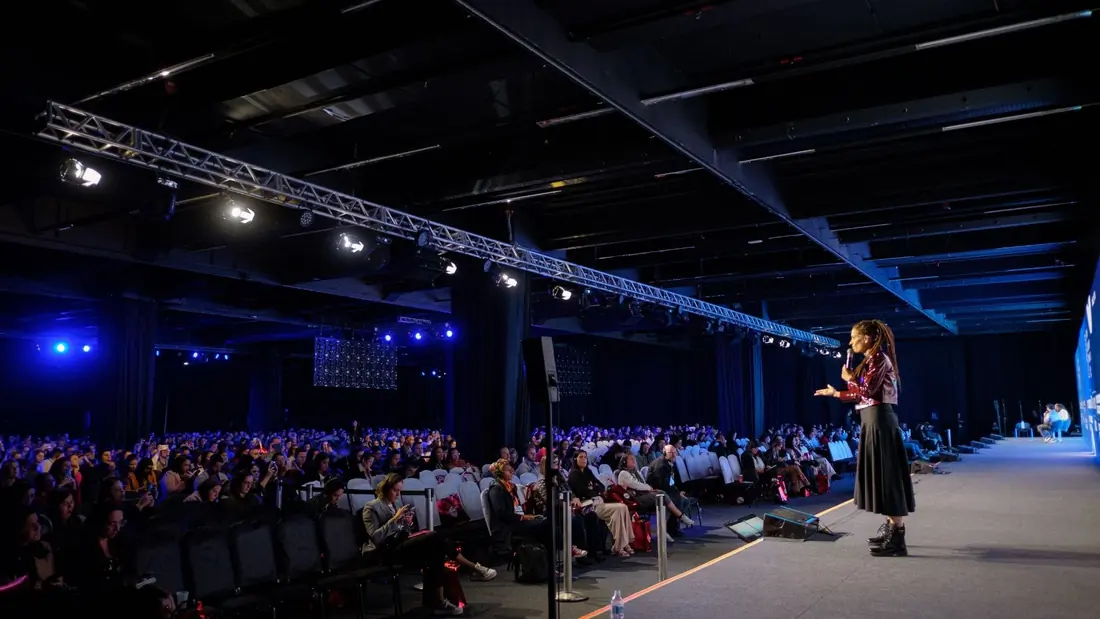 Monica Magalhaes standing at the tip of the stage runway, with the audience seated to the left