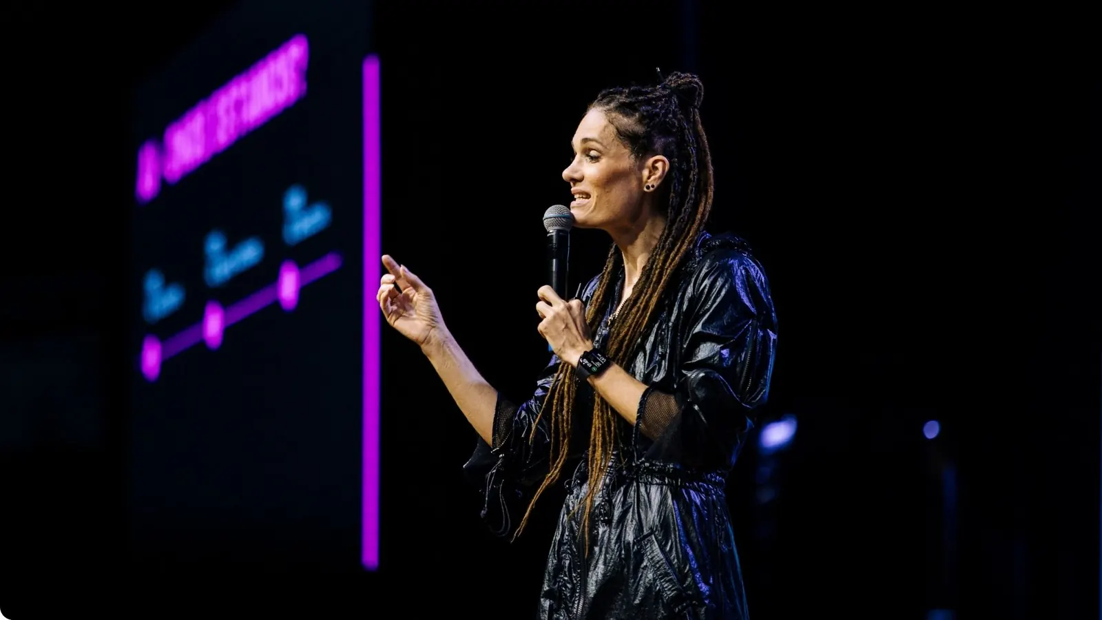 Monica Magalhaes at the microphone on stage, with a slide projected behind her