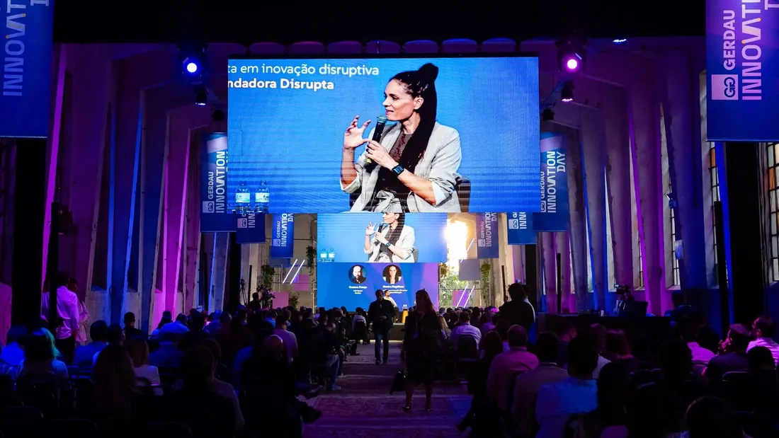 Monica Magalhaes on a panel, with her image projected on two large screens above the audience